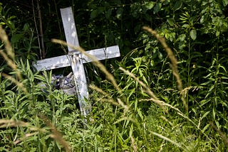 weathered wooden cross surrounded by weeds