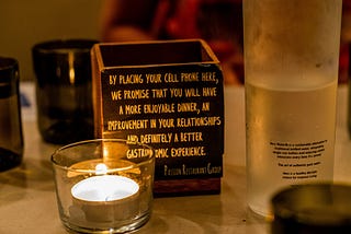 A brand taking a stand — tealight candle beside brown wooden box The cell phone rest box in Crazy About You restaurant. The box reads: By placing your cell phone here, we promise that you will have a more enjoyable dinner, an improvement in your relationships, and definitely a better gastronomic experience.