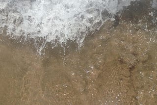 Woman’s feet standing on the edge of the ocean waves.