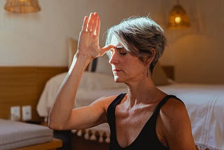 Mature woman with short gray hair meditating in her bedroom.