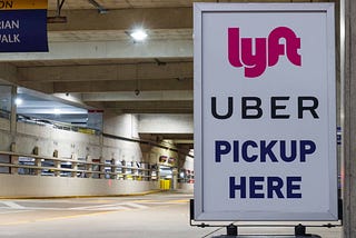 Rideshare pick up area; sign reads: “Lyft. Uber. Pickup Here.”