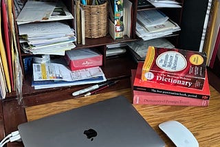 A desk with an Apple laptop, a dictionary, and grammar books.