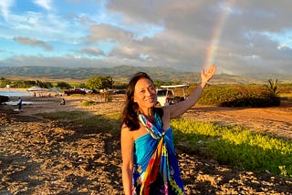Woman with upraised hand receiving a rainbow coming down from the sky