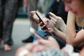 people sitting next to each other outside, looking at their phones