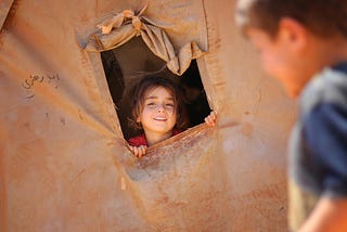 smiling little ethnic girl looking out of window in tent (description from picture source)