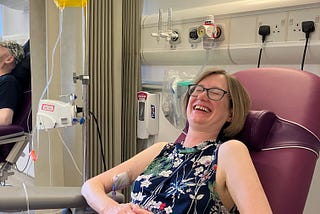 A woman in a hospital chair with an IV in her arm, laughing