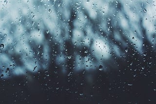 Rain drops through a window looking out at blurred trees