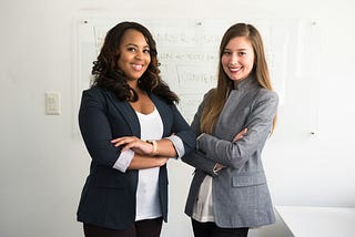 Two women in business attire, posing with arms crossed and smiling