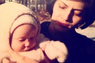 My mom is holding me as a baby; I have on a fleece onsie. Judging by the age and the backdrop of denuded trees, I think we’re in Waltham, Mass.