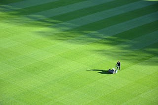 Picture of a person with a push mower, mowing a very large lawn.