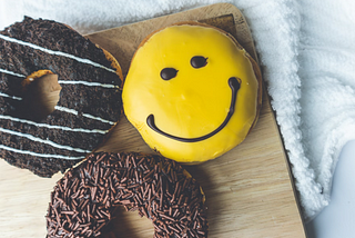 A yellow chocolate donut on a bed