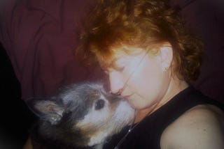 A woman wearing nasal prongs, cuddling a dog