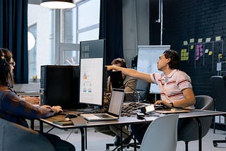 Three programmers working together with one pointing out something on the other’s screen