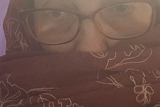 photo of the author’s head and shoulders, swathed in a dark burgundy scarf embroidered with large outlines of flowers in white thread, not for religious or cultural reasons, but because I’m cold.