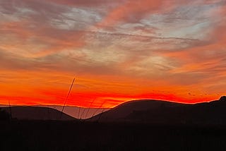 Bright orange sunset above soft curves of darkened hills