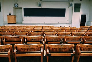 empty auditorium with wooden chairs, podium, and chalkboard