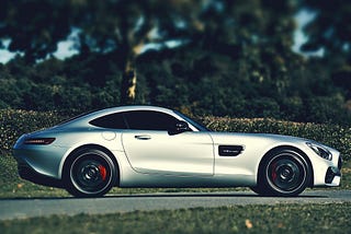 A sexy Silver Mercedes in profile against a backdrop of a hedge and green trees.