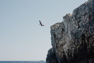 person jumping off a cliff into the ocean