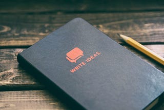 Notebook titled “Write Ideas,” next to a pencil on a wooden table top.