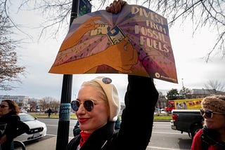 A woman holds up a sign that reads, “Divest from Fossil Fuels.”