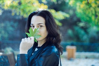 A peacefully happy woman holding a maple leaf in front of her smile