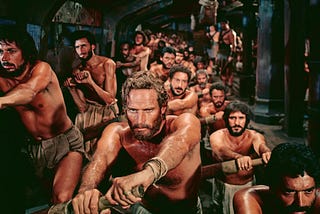 A scene from the 1959 film Ben-Hur in which Charlton Heston in the title role is one of a large group of slaves forced to row a Roman galley.