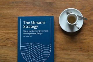 A book “The Umami Strategy” on a wooden tabletop with a white coffee cup next to it.