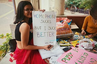 Picture of me holding a placard that reads ‘Homophobia sucks but I suck better’ before I and my college mates went to the Annual Delhi Queer Pride of 2019