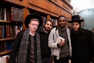 A group of four men of varying skin shades, dressed mostly in black, in a library as part of their pilgrimage to Israel.