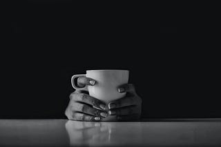 Two hands holding a coffee mug against a black background