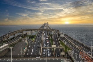 Traffic jam on the Tokyo Bay Aqua Line highway at sunset during a busy three-day holiday in Japan, with cars lined up across the bridge spanning the bay.