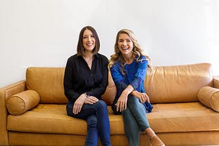 Equip co-founders Dr. Erin Parks and Kristina Saffran sitting on a tan colored couch together, smiling and laughing.