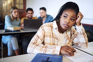 Image of a young, black girl looking into the distance with a sad look mid-study, with three white students blurred in the background and studying together