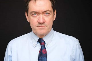 Image shows James Bullion, Chief Inspector of Adult Social Care and Integrated Care, CQC. James is against a black background, and is wearing a blue shirt with a blue and red tie.