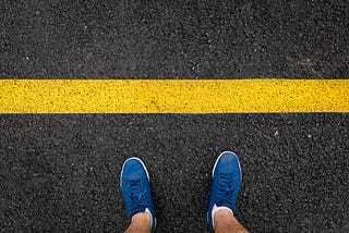 person looking down at shoes standing before a yellow line