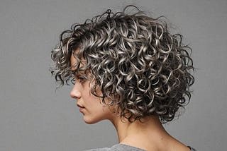 Image shows a grey background and a woman with curly hair seen from the side in the middle of the image.