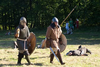 The explorer that stopped 5 minutes before the miracle. nicole wallet. two men dressed in Viking clothing carry shields and swords across a field, reincting a Viking battle.