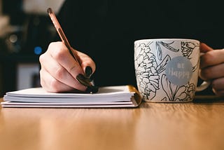 woman writing in journal with coffee mug in other hand