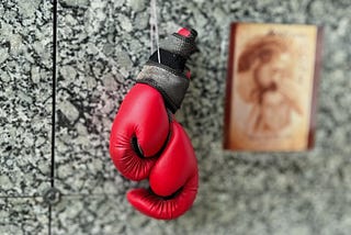 photo of a pair of bright red boxing gloves hanging on a gravestone next to a faded illustration of Jesus