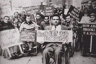 Black-and-white photograph of disabled World War II veterans in wheelchairs protesting on a New York City sidewalk, holding handmade signs reading ‘Don’t Let Us Down,’ ‘Keep Faith With Disabled Vets,’ and ‘Don’t Break Promises.