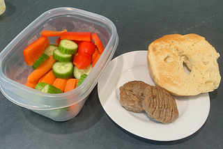 Photo of chopped vegetables, a bagel, and breakfast sausage.