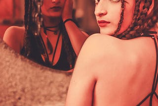 Girl sitting in front of a mirror that reflects a different version of her.