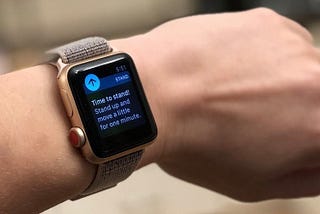 A worn Apple Watch displaying a “Time to stand!” notification