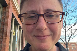 The author is smiling into the camera. He is white and trans. He looks a little tired, but otherwise relaxed. He’s wearing glasses.
