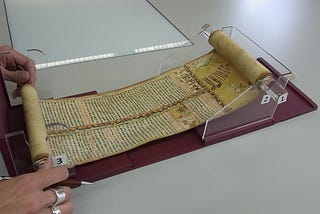 Ethiopian scroll being displayed on Wellcome’s custom-made scroll holder, made of clear plastic. Two hands are unravelling the scroll.
