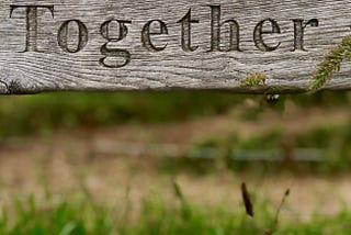 A wooden fence in front of a field with the word “together” etched into the surface.