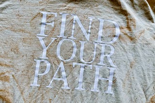 A dirt-washed T-Shirt with large, white block letters reading: “FIND YOUR PATH”