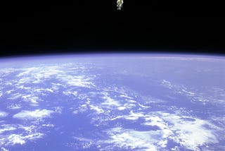 Astronaut Bruce McCandless pictured floating in space powered by a nitrogen jetpack. The bright blue earth can be seen in the bottom half of the picture, with the dark abyss of space above.