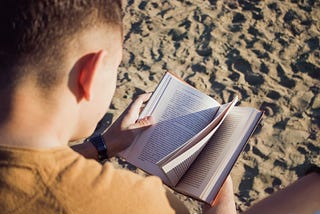 A man sits on the beach with an open book.