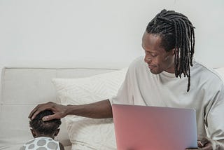 Father kindly caressing toddler while working on laptop.